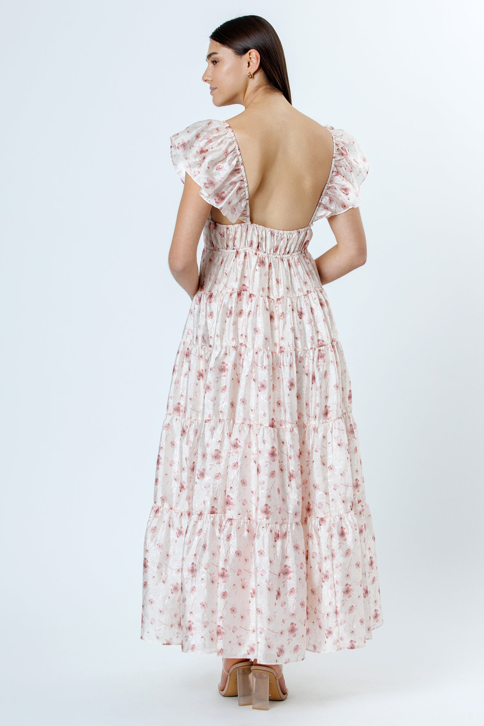Back view of a woman wearing a floral dress with a backless design on a white background