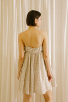 Back view of a woman wearing a beige mini dress against a beige curtain background
