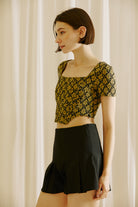 Side view of a woman wearing a floral top and black shorts against a beige curtain background