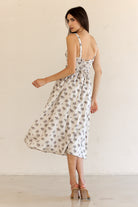 Back view of a woman wearing a beige floral dress against a plain background