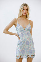 Woman wearing a blue and mint floral lace dress against a white background