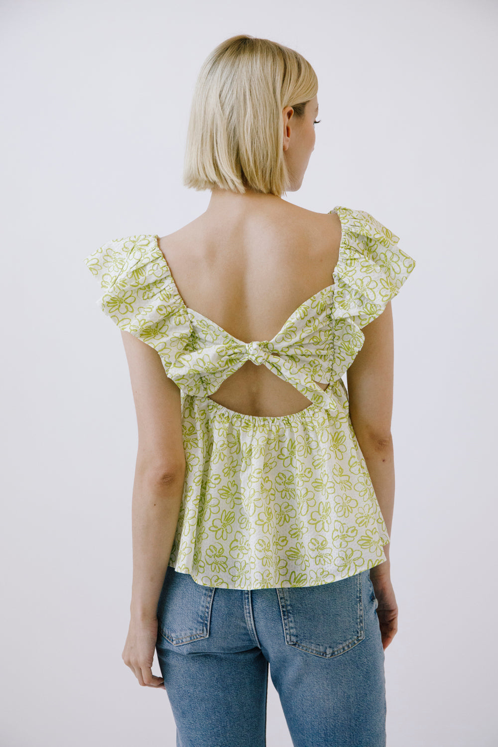 Woman wearing a light green floral top with a bow back design on a white background