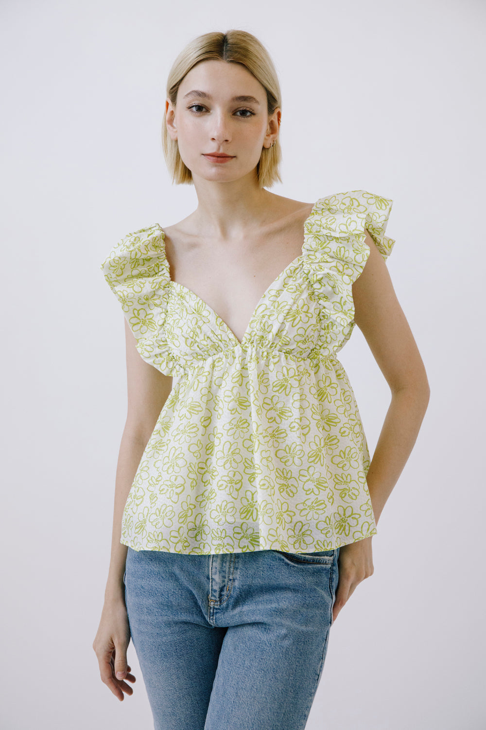 Woman wearing a green floral top and blue jeans against a white background