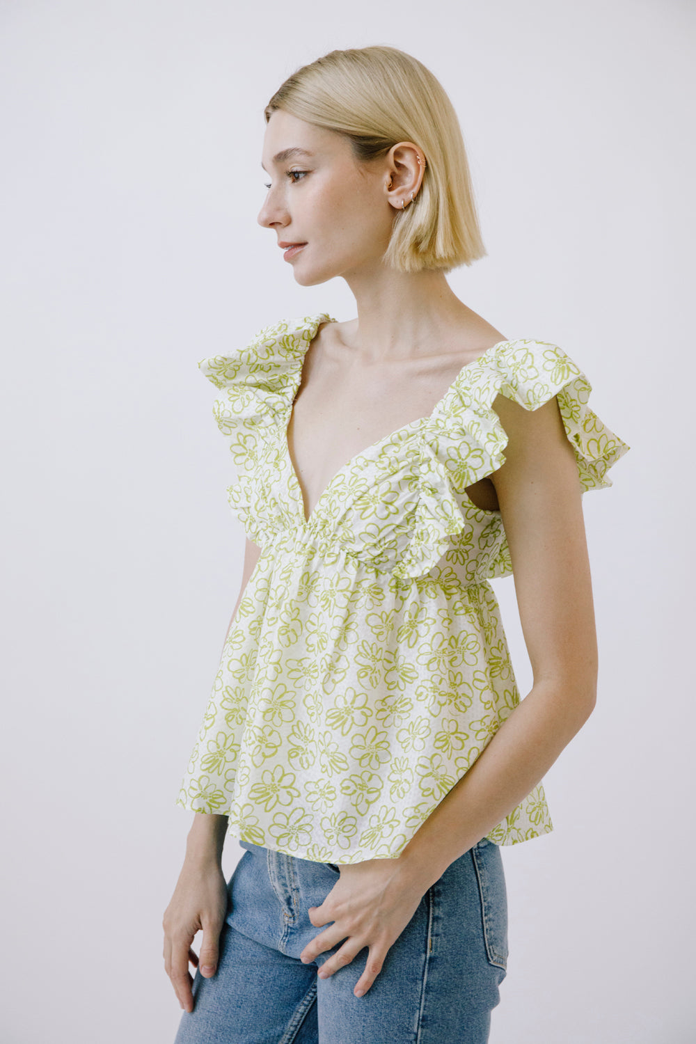 Side view of a woman wearing a light green floral blouse with ruffled sleeves against a white background