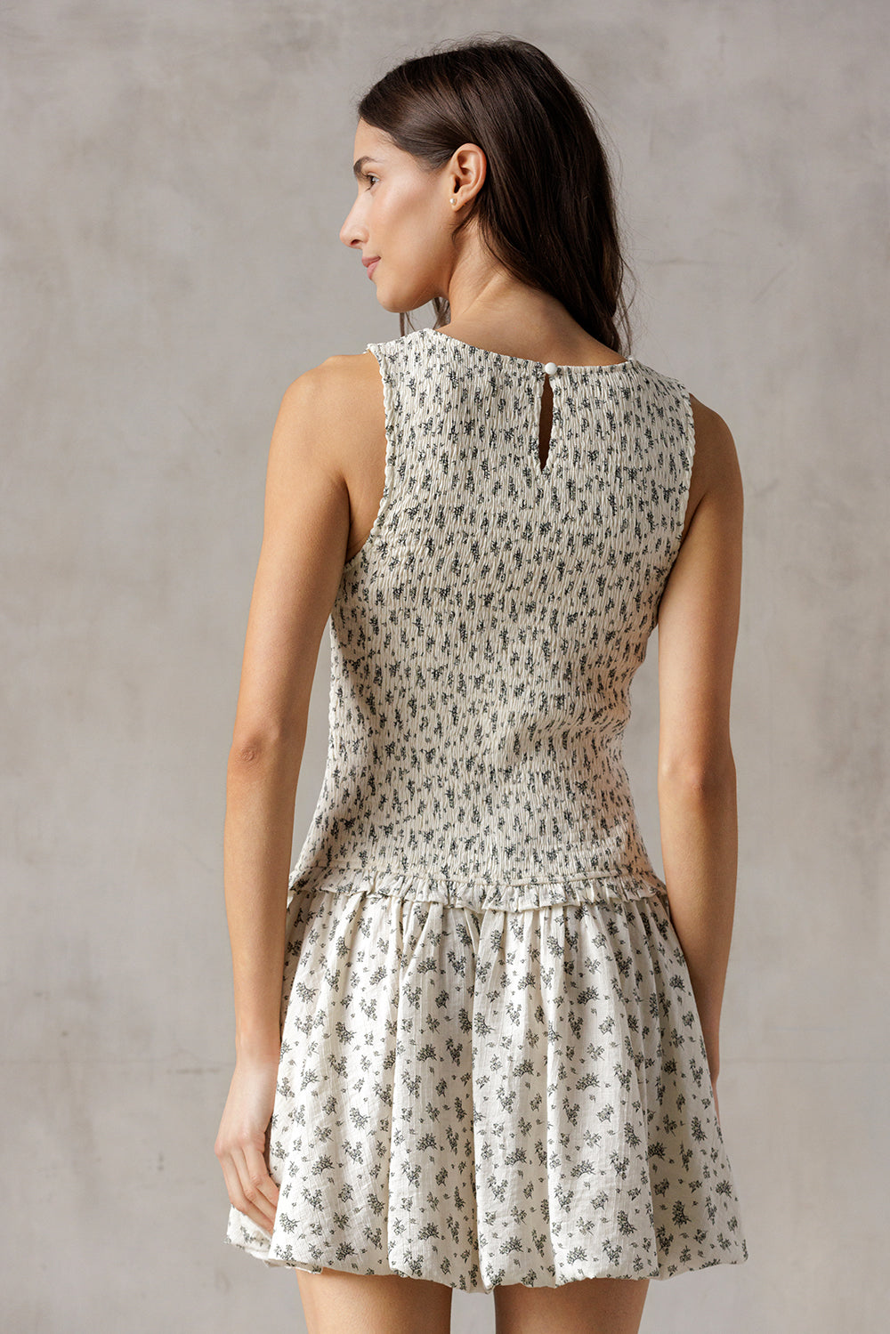 Back view of a woman wearing an ivory floral dress against a gray background