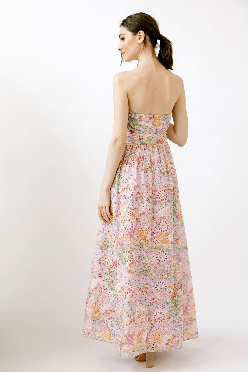 Back view of a woman wearing a colorful floral print strapless dress on a white background
