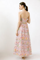 Back view of a woman wearing a colorful floral print strapless dress on a white background