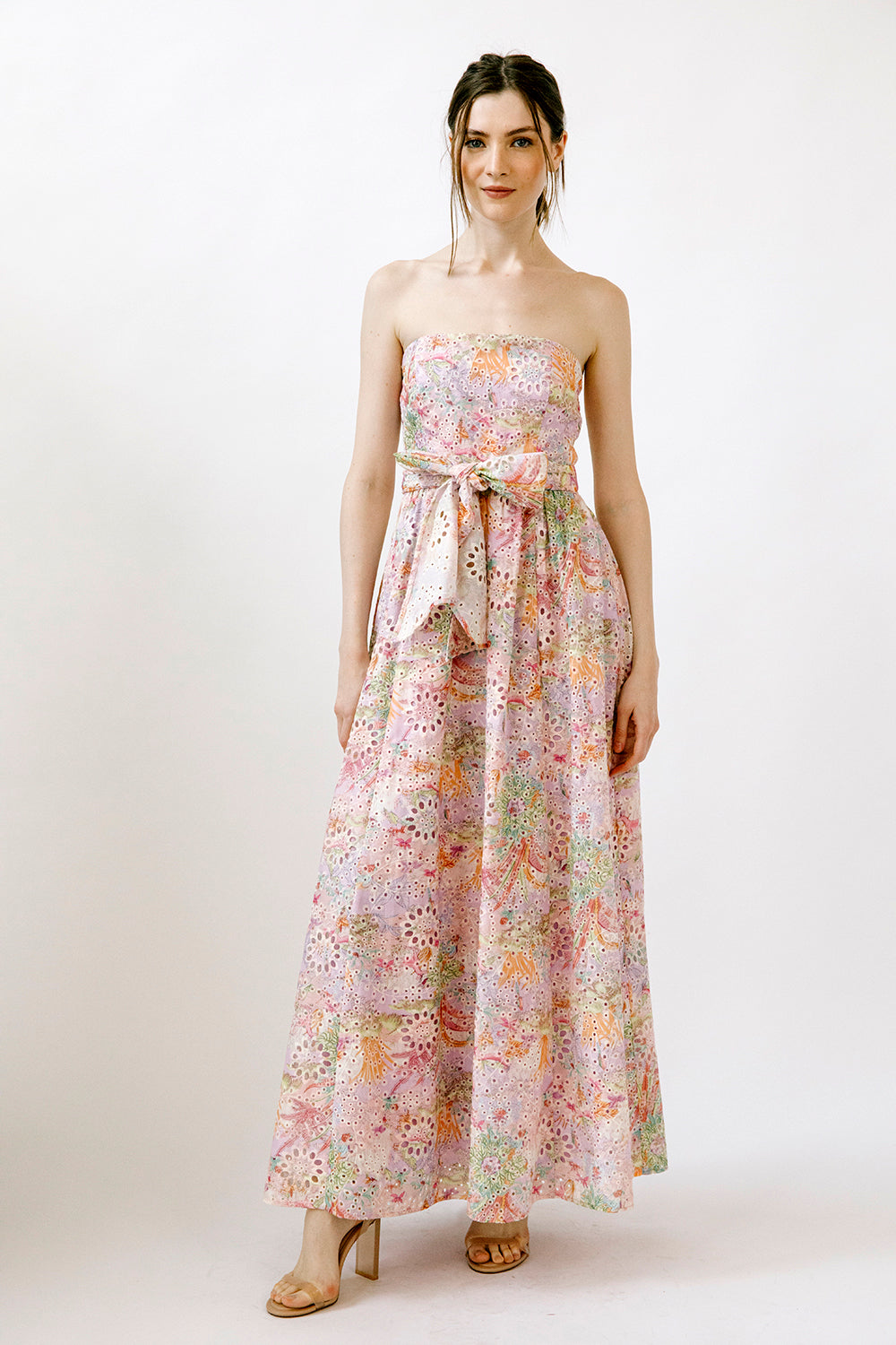 Woman wearing a colorful floral print on embroidered eyelet fabric strapless dress on a white background