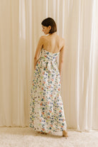Back view of a woman wearing a blue floral strapless dress against a beige curtain background