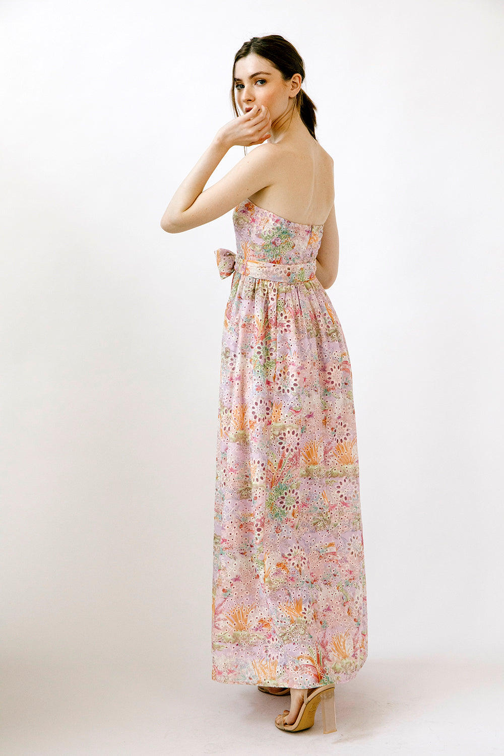 Side view of a woman wearing a colorful floral print on embroidered eyelet fabric dress on a white background