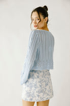 Back view of a woman wearing a blue knit cardigan with lace-up details and a toile print skirt on a white background