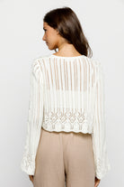 Woman wearing a white knit cardigan and beige pants on a plain background