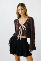 Woman wearing an eggplant knit cardigan with lace-up details and a black pleated skirt on a white background
