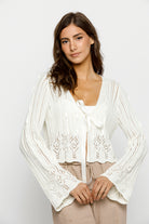 Woman wearing a white knit cardigan against a plain background