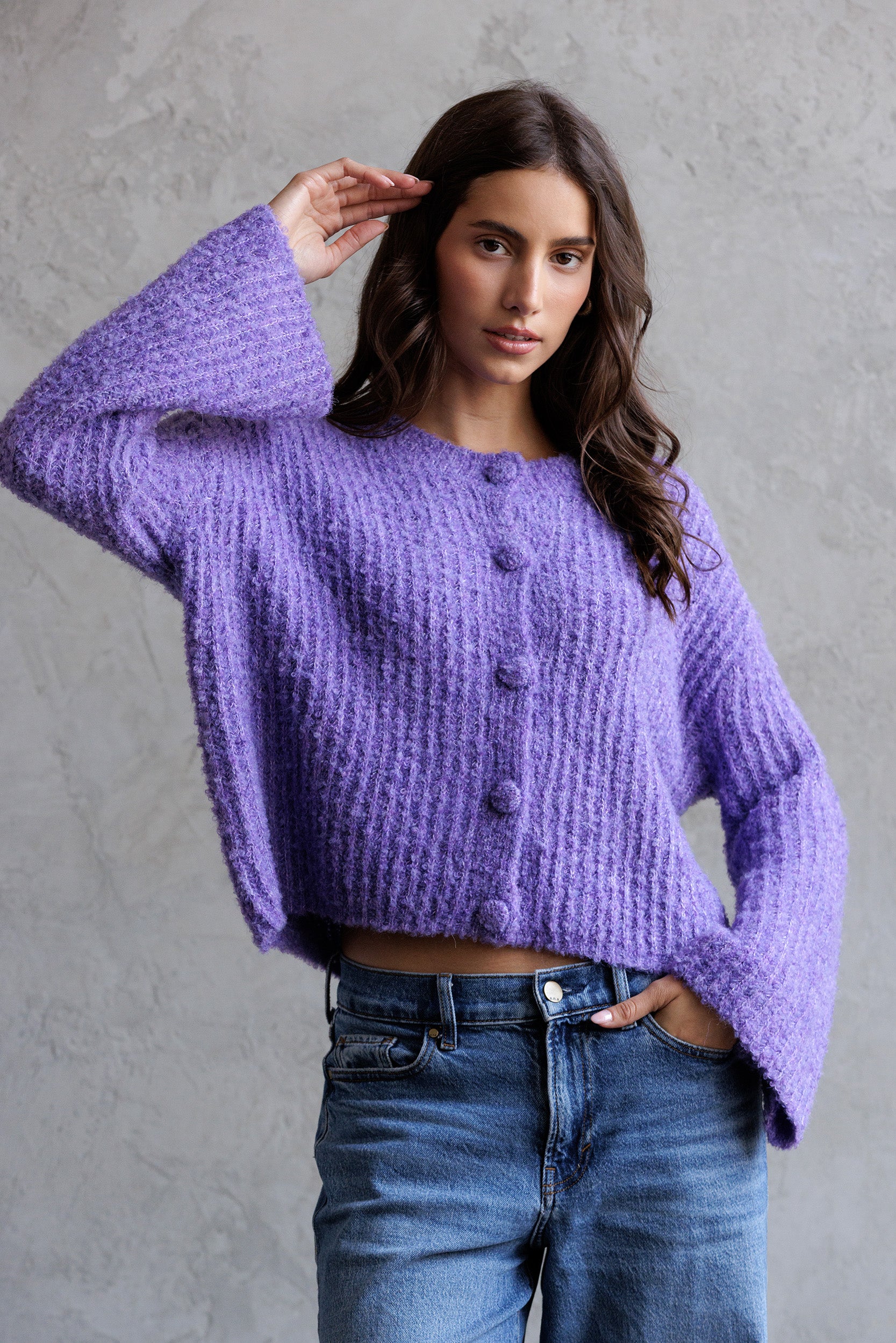 Woman wearing a purple sweater and blue jeans against a gray background
