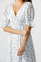 White dress with blue floral pattern worn by a person on a plain background