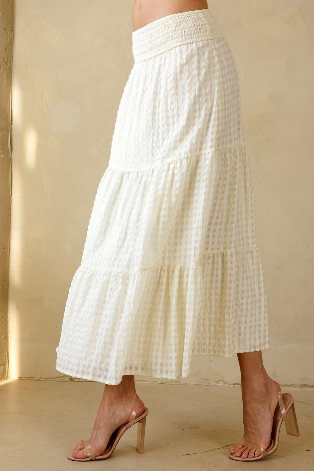 Side view of a cream maxi skirt with a subtle checkered pattern worn by a person on a beige background