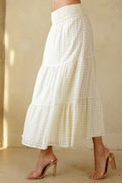Side view of a cream maxi skirt with a subtle checkered pattern worn by a person on a beige background