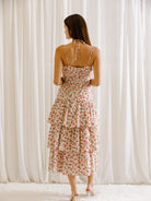 Back view of a woman wearing a floral dress with ruched upper body standing against a white curtain