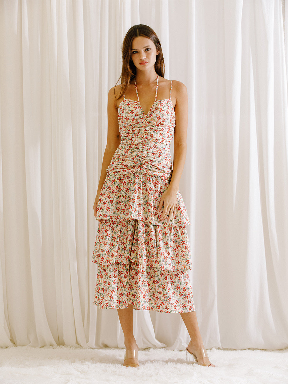 Woman wearing a floral dress with ruched upper body standing against a white curtain