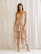 Woman wearing a floral dress with ruched upper body standing against a white curtain