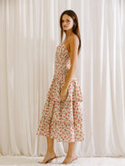 Side view of a woman wearing a floral midi dress with ruched upper body standing against a white curtain