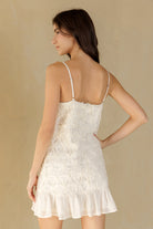 Back view of a woman wearing a white 3D floral dress against a beige background