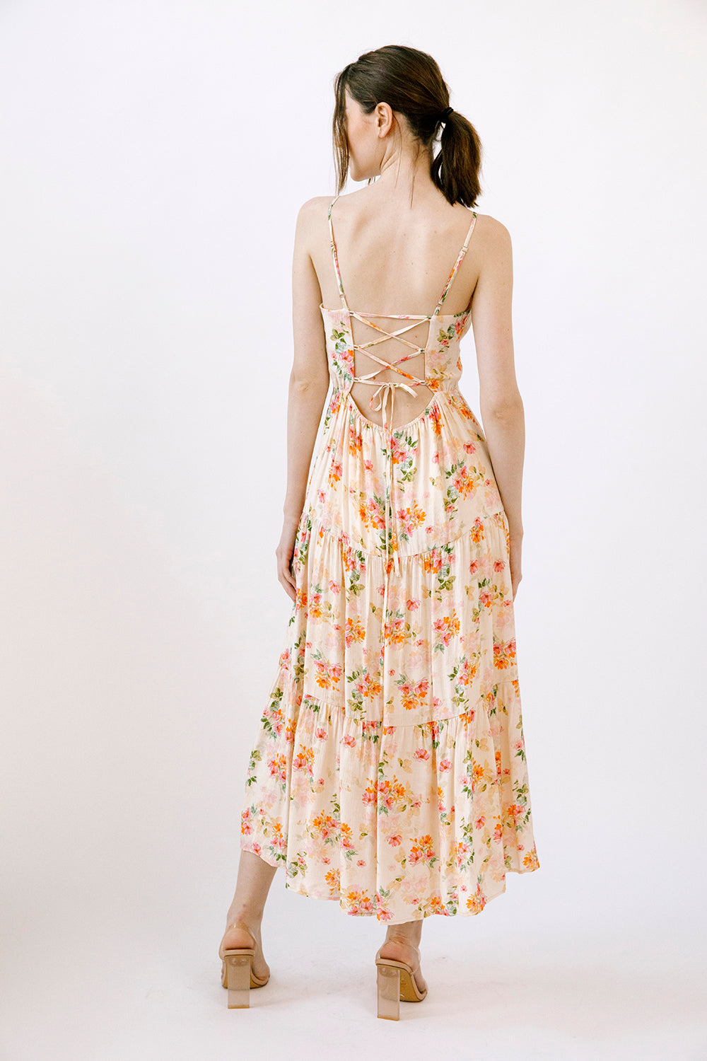 Back view of a woman wearing a cream dress with a watercolor-inspired floral pattern on a white background