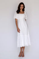 A model wearing a romantic white cotton midi dress with embroidered details, puff sleeves, and a scalloped eyelet hem for timeless everyday style.