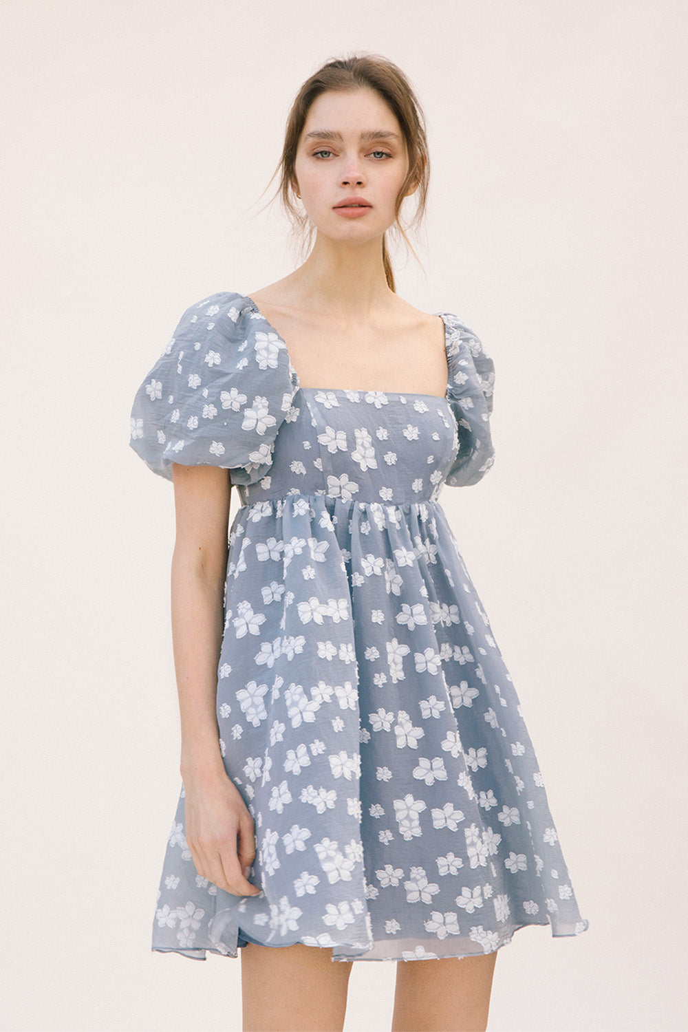 Woman wearing a blue dress with white floral embroidery and puff sleeves on a white background