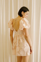 Back view of a woman wearing a peach dress against a neutral wall.
