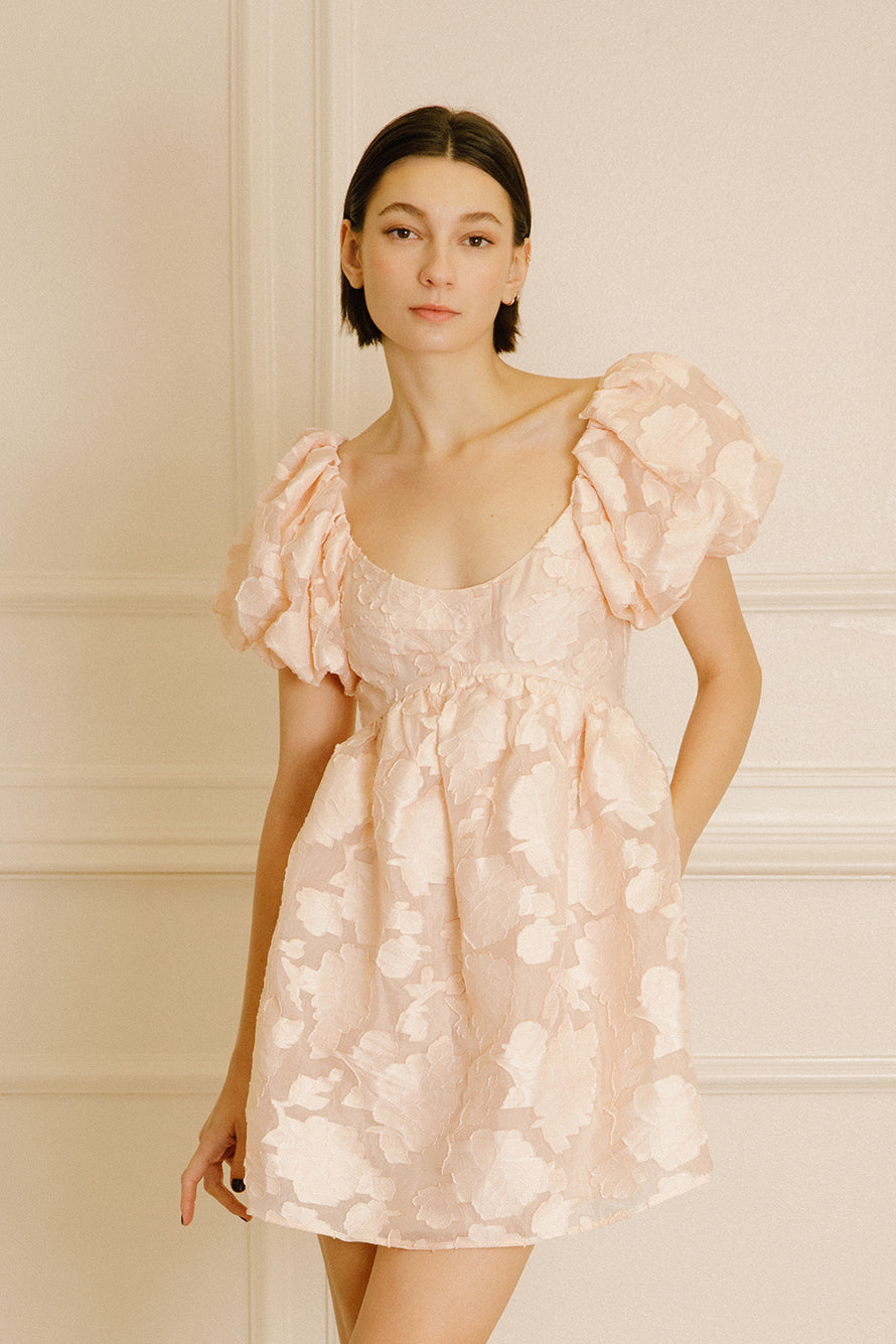 Woman wearing a peach dress against a neutral wall.