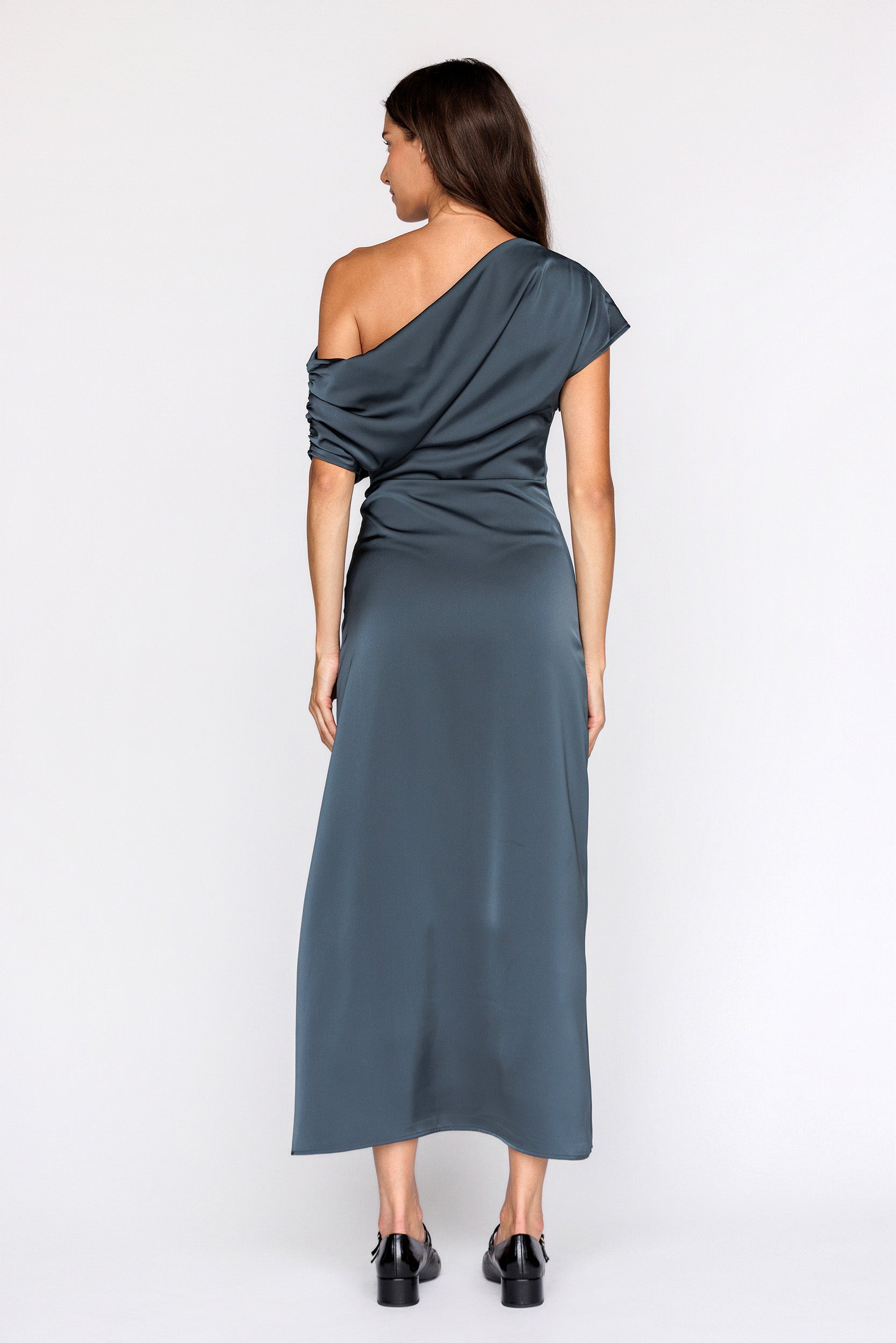 Back view of a woman wearing a teal one-shoulder dress on a white background