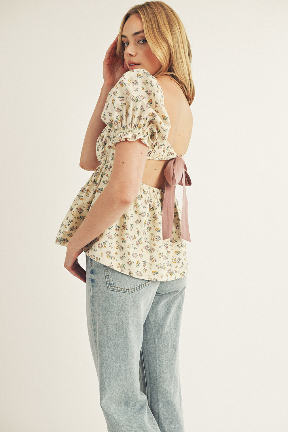 Side view of a model wearing a cream blouse with floral pattern and denim jeans