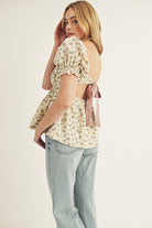 Side view of a model wearing a cream blouse with floral pattern and denim jeans