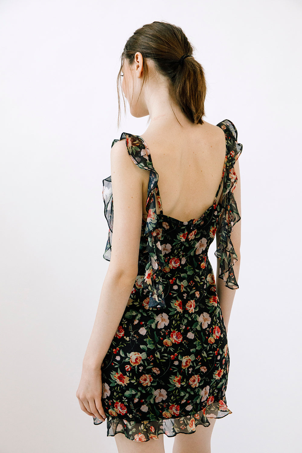 Woman wearing a floral dress with adjustable straps with ruffled details against a plain background