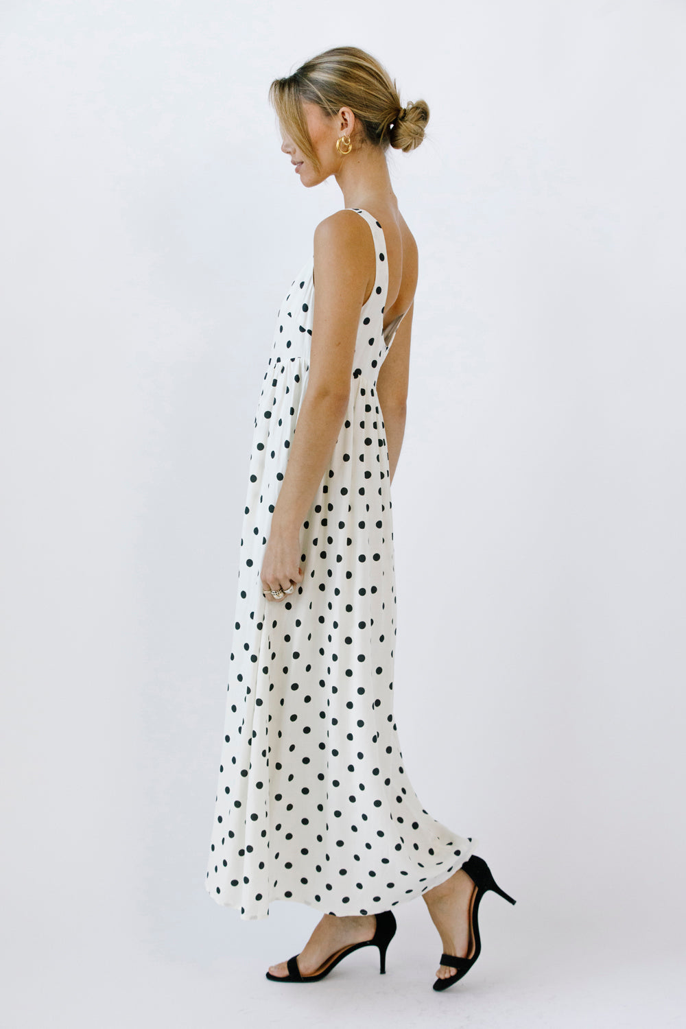 Side view of a woman wearing a polka dot maxi dress on a white background