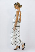 Side view of a woman wearing a polka dot maxi dress on a white background