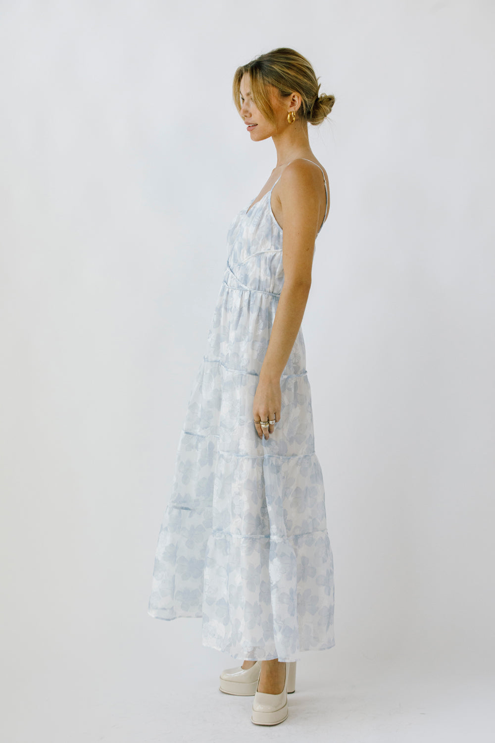 Side view of a woman wearing a light blue floral maxi dress on a white background