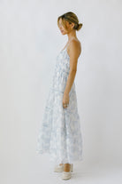 Side view of a woman wearing a light blue floral maxi dress on a white background
