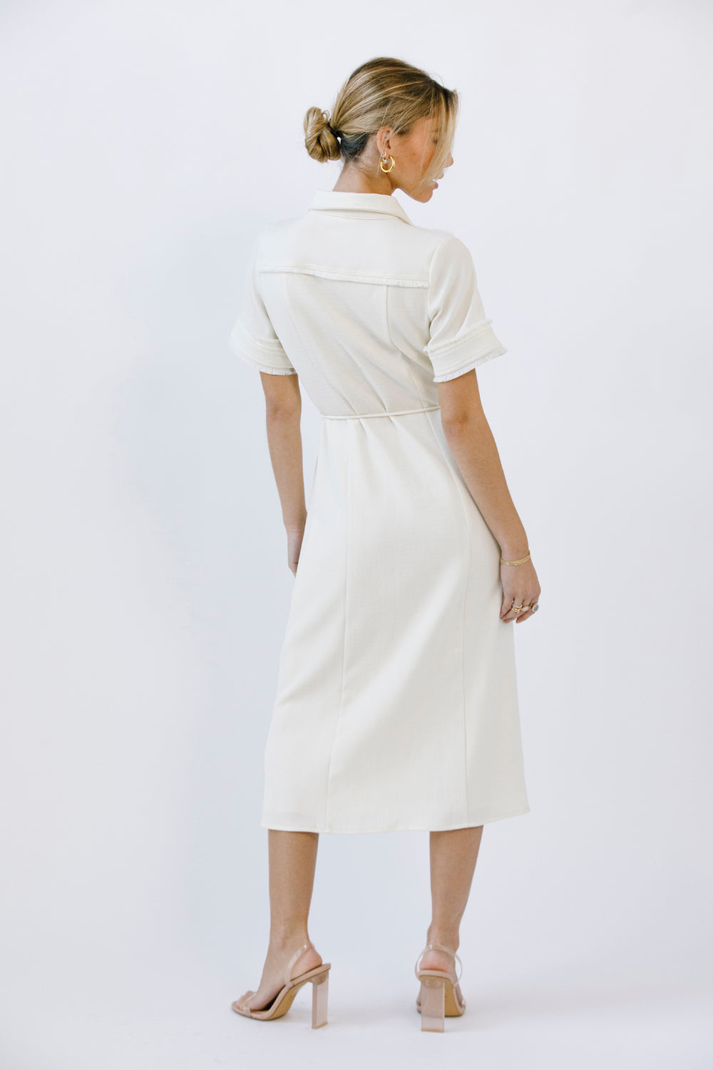 Back view of a woman wearing a cream dress on a white background