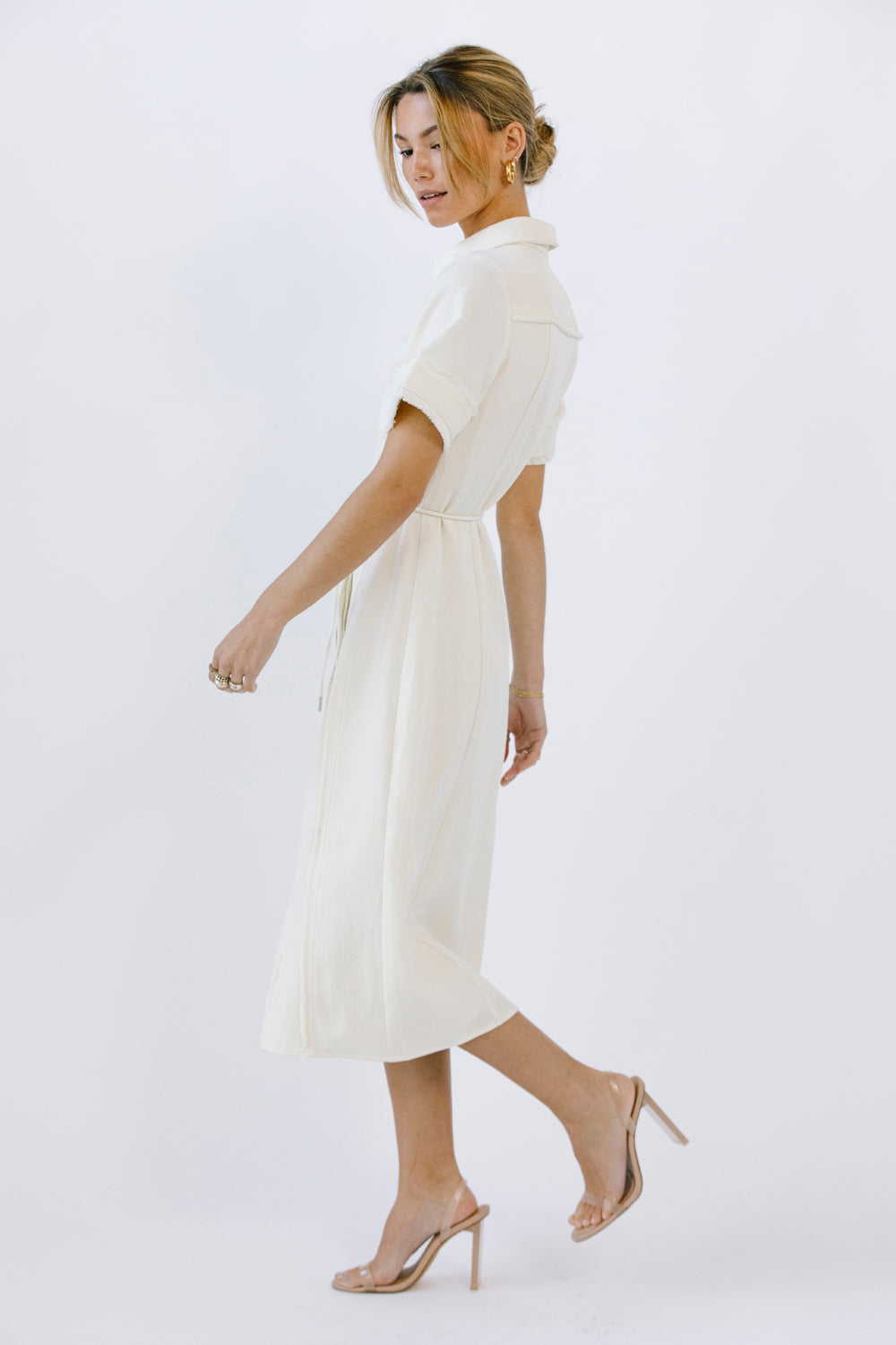 Side view of a woman wearing a cream dress and beige high-heels on a white background
