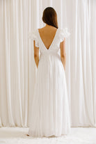 Back view of a woman wearing a white maxi dress standing against a white curtain