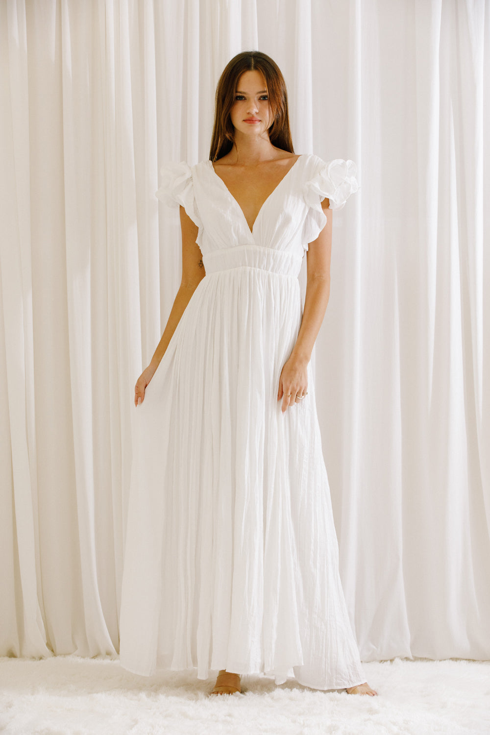 Woman wearing a white maxi dress standing against a white curtain