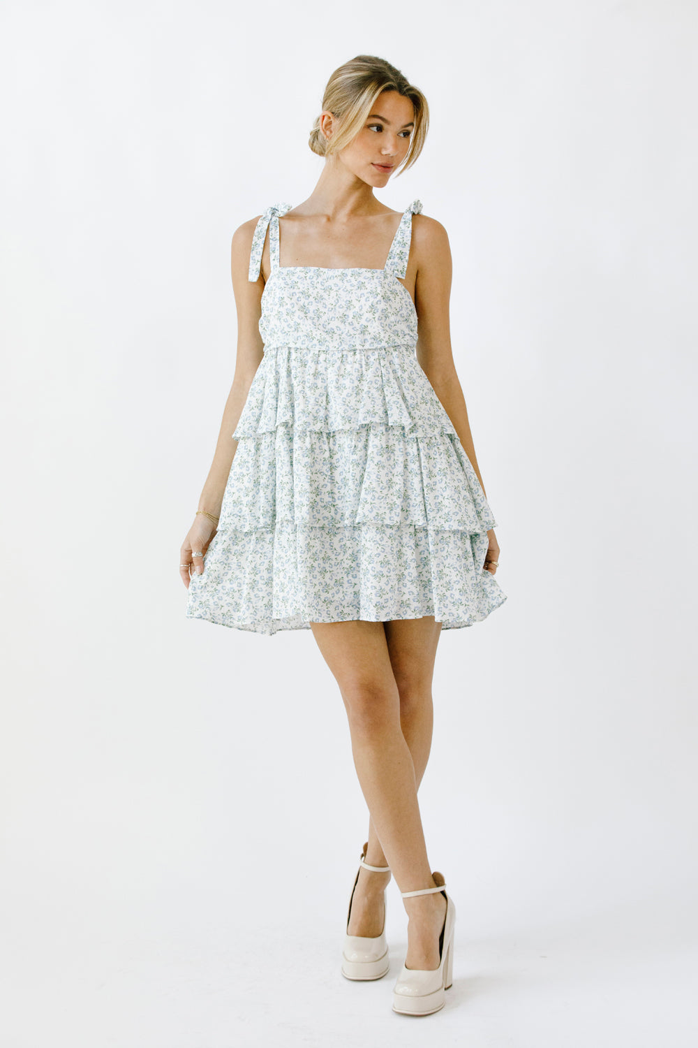 Woman wearing a floral dress with a tiered ruffle design and beige high-heels on a white background