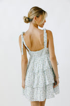 Back view of a woman wearing a floral dress with a tiered ruffle design on a white background