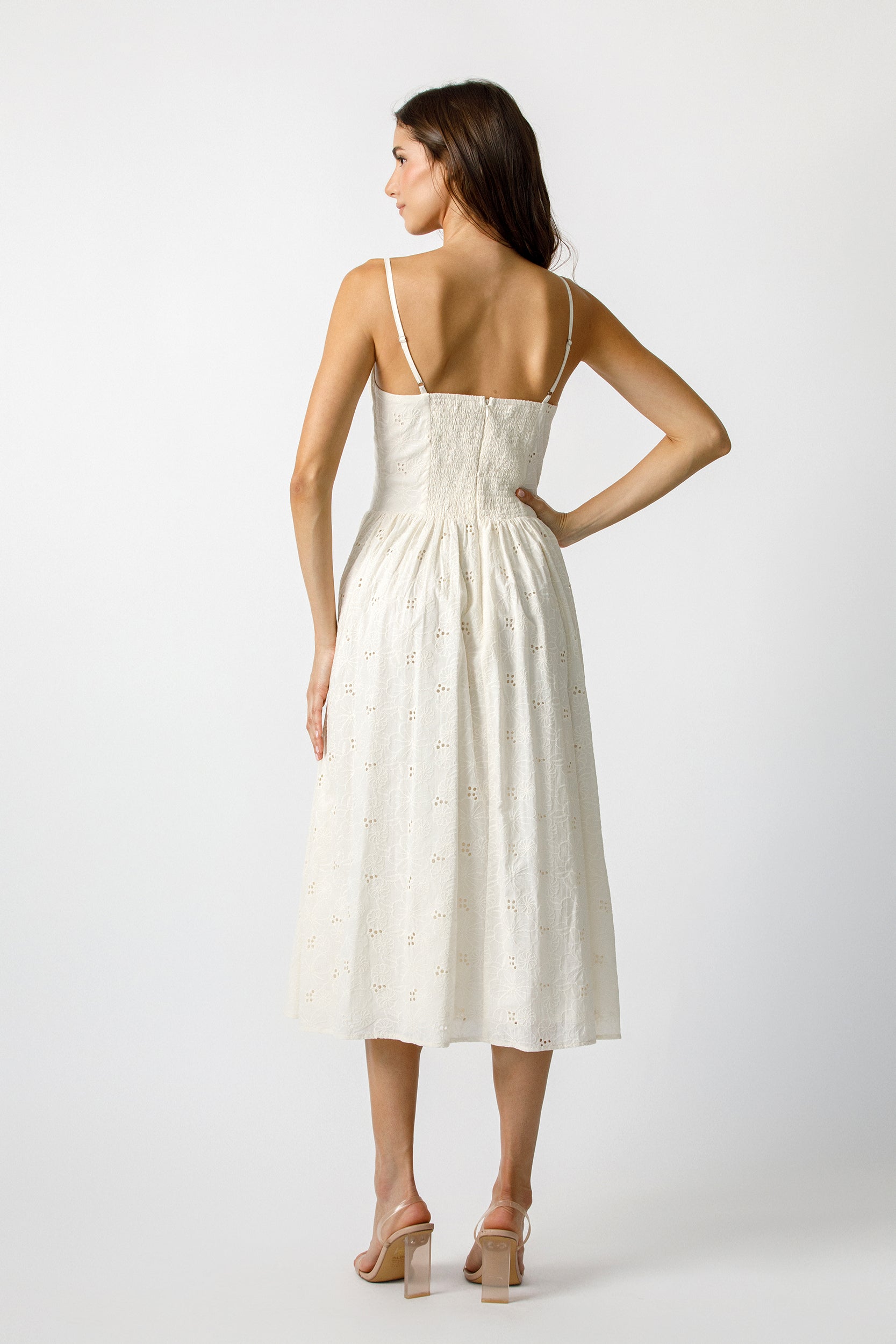 Back view of a woman wearing a cream dress with eyelet details on a plain background