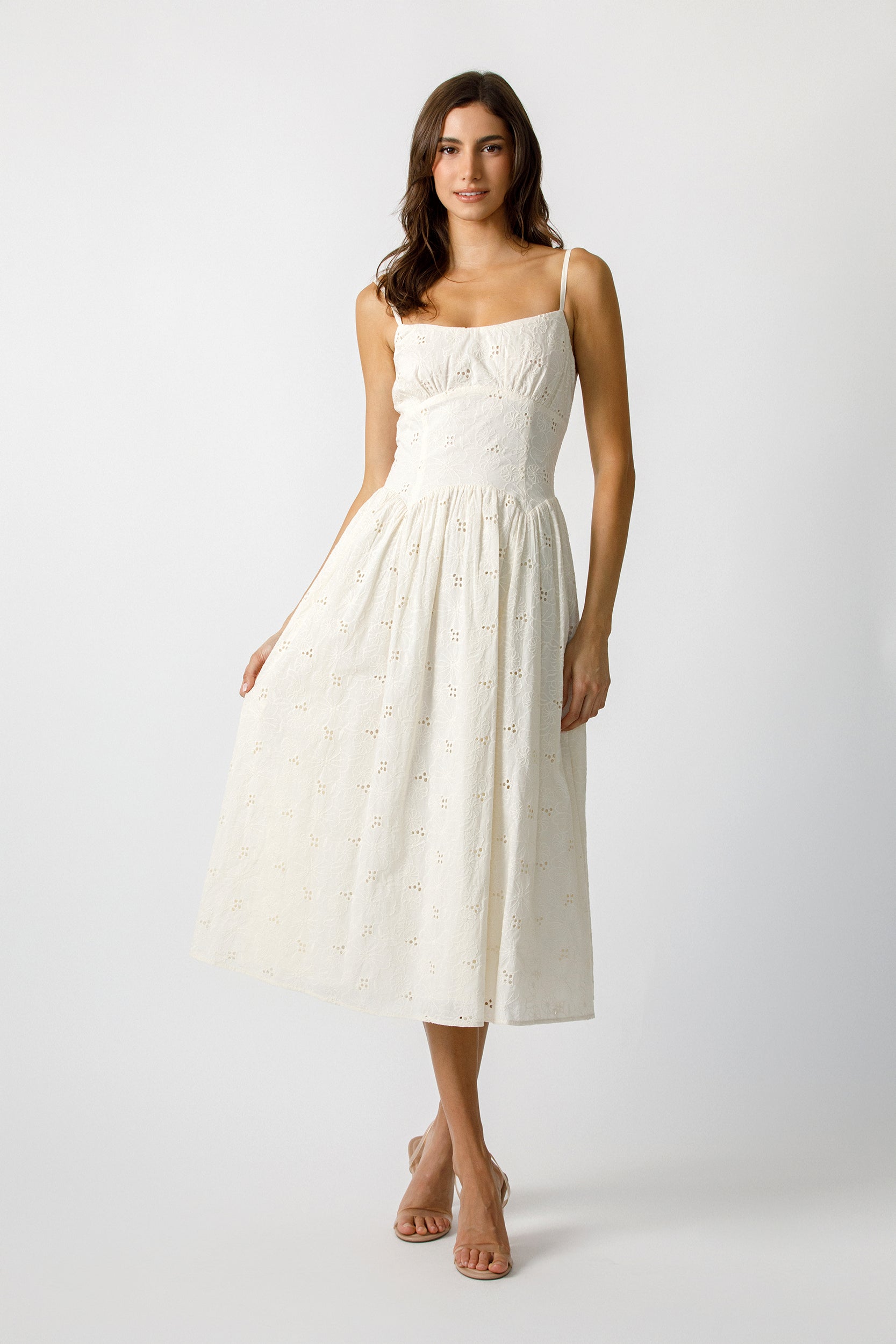 Woman wearing a cream dress with eyelet details on a plain background
