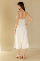Back view of a woman wearing a cream midi dress against a beige background