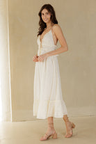 Woman wearing a cream midi dress with floral embroidery against a beige background